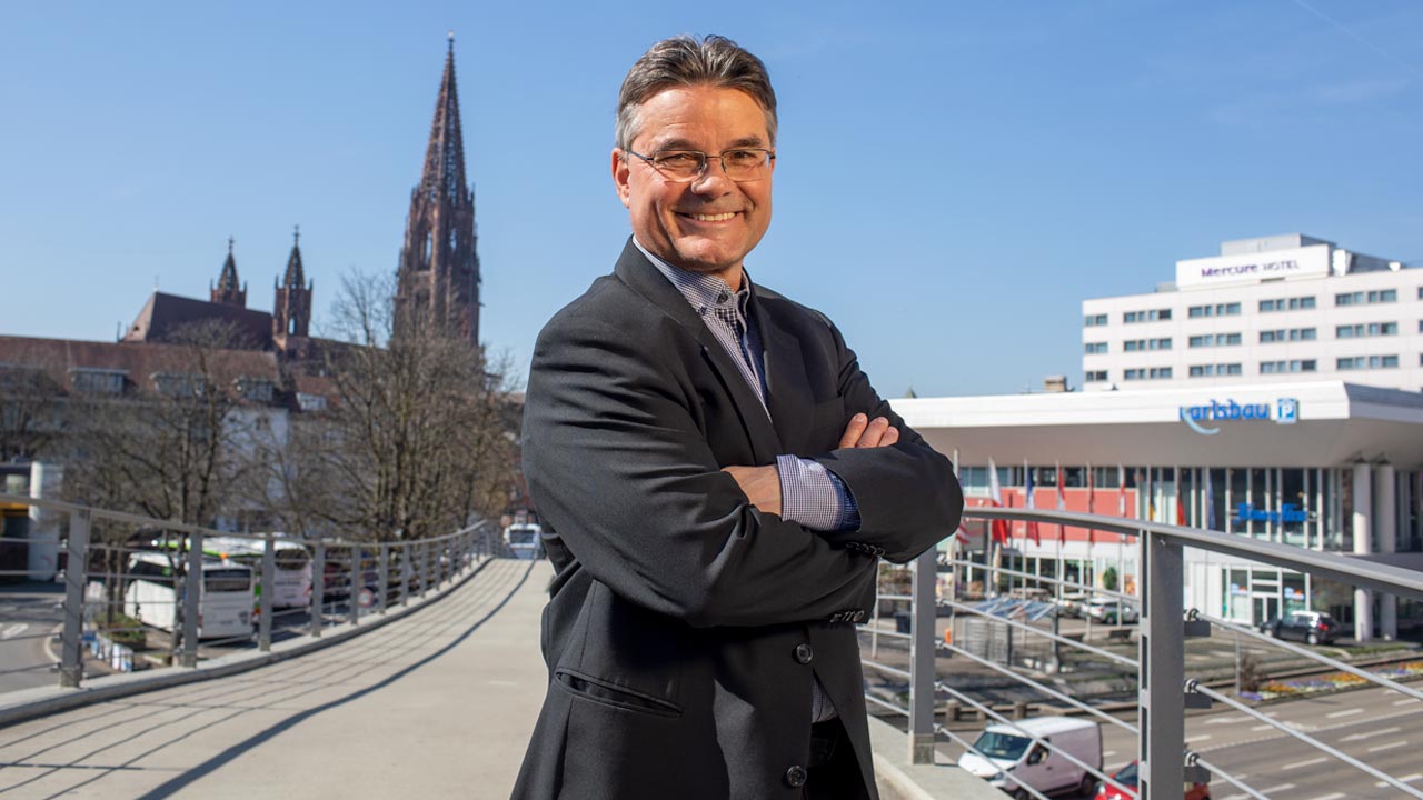 Das Foto zeigt den kaufmännische, Geschäftsführer Ralf Klausmann auf der Fußgängerbrücke zum Stadtgarten. Im Hintergrund ist das Freiburger Münster zu sehen.