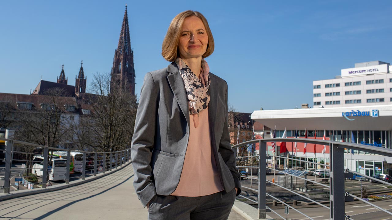 Das Foto zeigt die technische Geschäftsführerin Dr. Magdalena Szablewska auf der Fußgängerbrücke zum Stadtgarten. Im Hintergrund ist das Freiburger Münster zu sehen.